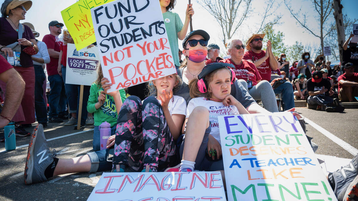 Katie Ragle sits with her daughters Eliana, left and Delilah, right with pink headphones as they support their teachers at Alice Birney Waldorf Inspired K-8 School in Sacramento in front of the Serna Center on Wednesday, March 23, 2022 during the start of the Sacramento City Teachers Association strike.