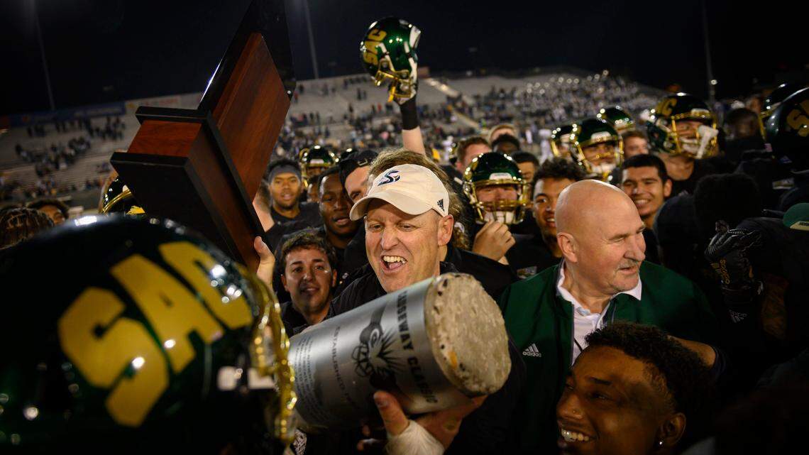 Sac State head coach Troy Taylor celebrates while being handed the Causeway Classic trophy while surrounded by the Hornets after their win Saturday, Nov. 23, 2019, during the 66th Causeway Classic against UC Davis at Hornet Stadium.