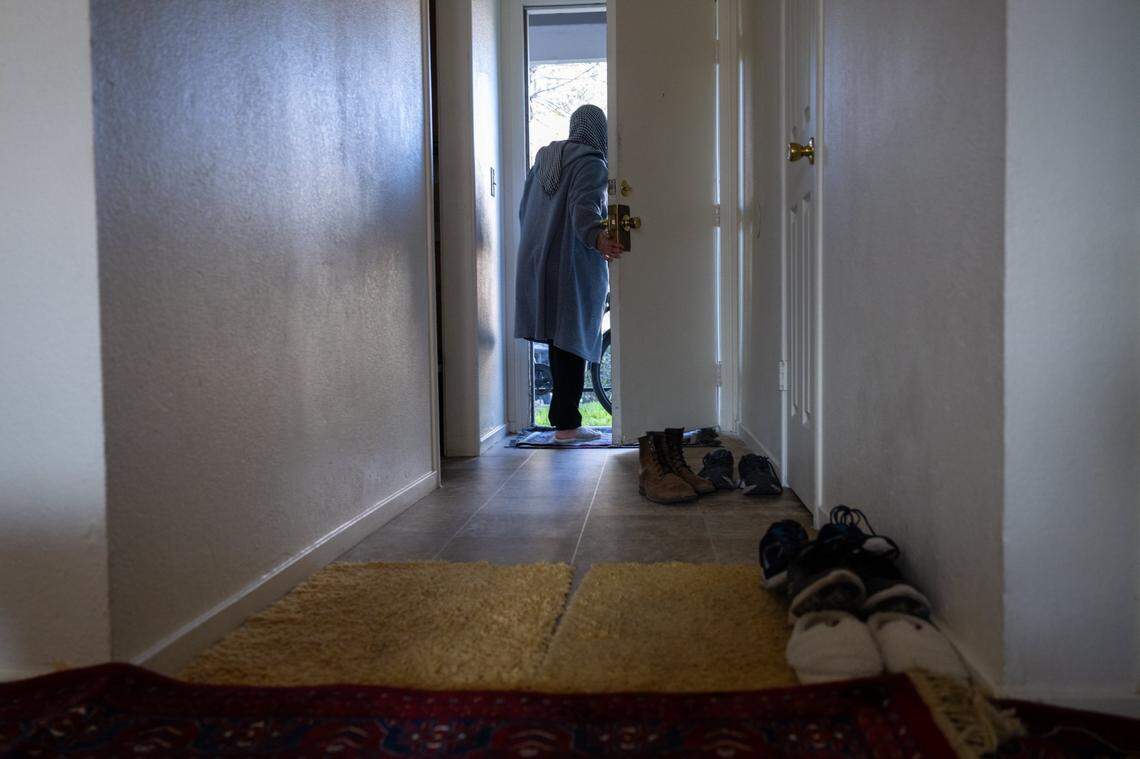 Shoes line the hallway as Marzia Ahmadi looks out the front door of her family’s Yuba City apartment last month. 