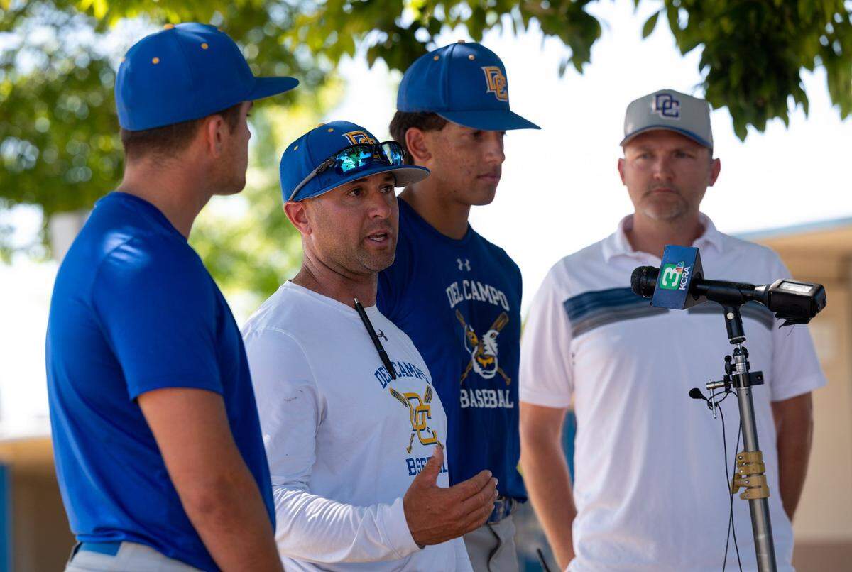 Del Campo High School baseball coach Kevin Dawidczik, flanked by players Luke Tuter and Jordan Jacobson, and joined by Principal Greg Snyder, right, talks Wednesday, May 18, 2022, in Fair Oaks about his school’s protest of a Sac-Joaquin Section decision to require his team to forfeit its victory in the first game of its Division lll playoff series against Buhach Colony High School and ban fans from the remaining games.
