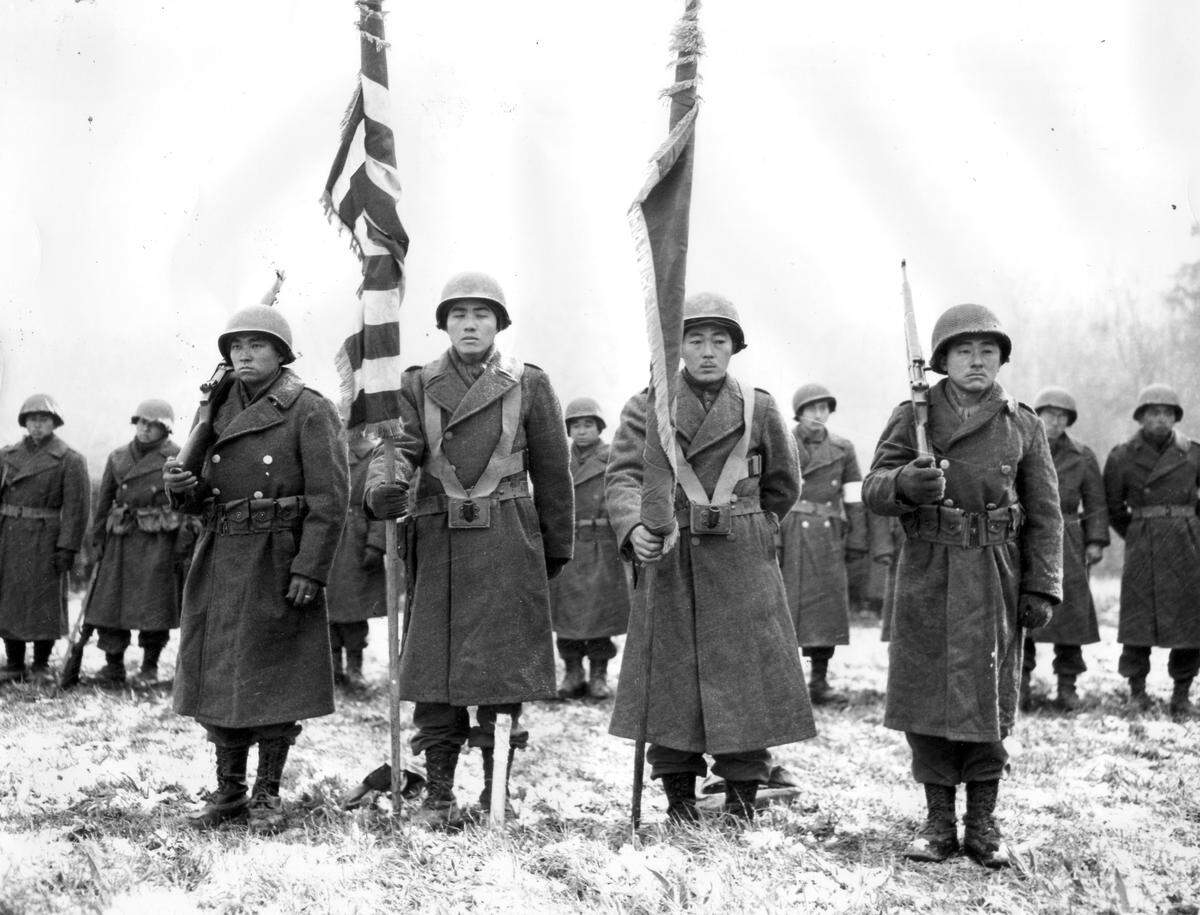 Two color guards and color bearers of the all-Japanese American 442nd Combat Team stand at attention while their citations are read on Nov. 12 1944. They are standing on ground in near Bruyères, France, where many of their comrades fell.