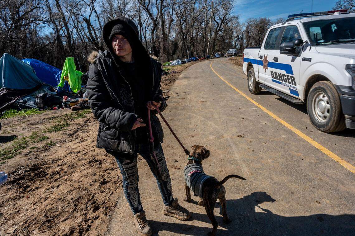 Michelle Standbridge waits with her dog for a hotel voucher as a ranger passes by near the Bannon Island encampment Thursday. “They really have hearts of gold and everybody doesn’t deserve to be out here,” she said about her fellow homeless campers.