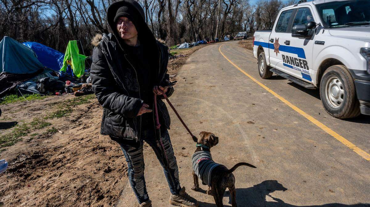 Michelle Standbridge, 40, waits with her dog for a hotel voucher on the brink of the Bannon Island encampment being swept in Sacramento on Thursday, March 2, 2023. “They really have hearts of gold and everybody doesn’t deserve to be out here,” she said about her fellow homeless campers.