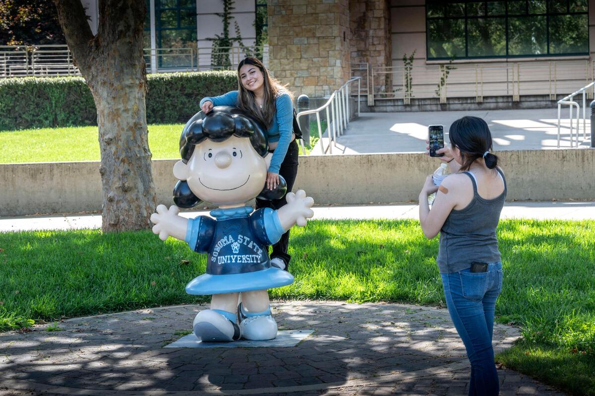 Abigail Alvarez, an incoming freshman at Sonoma State, poses for a photo on a statue of the “Peanuts” character Lucy near the Jean and Charles Schulz Information Center as her friend Mircka Garcia takes the picture on move-in day at the campus. Sonoma State lost a fifth of its enrollment over the past few years.