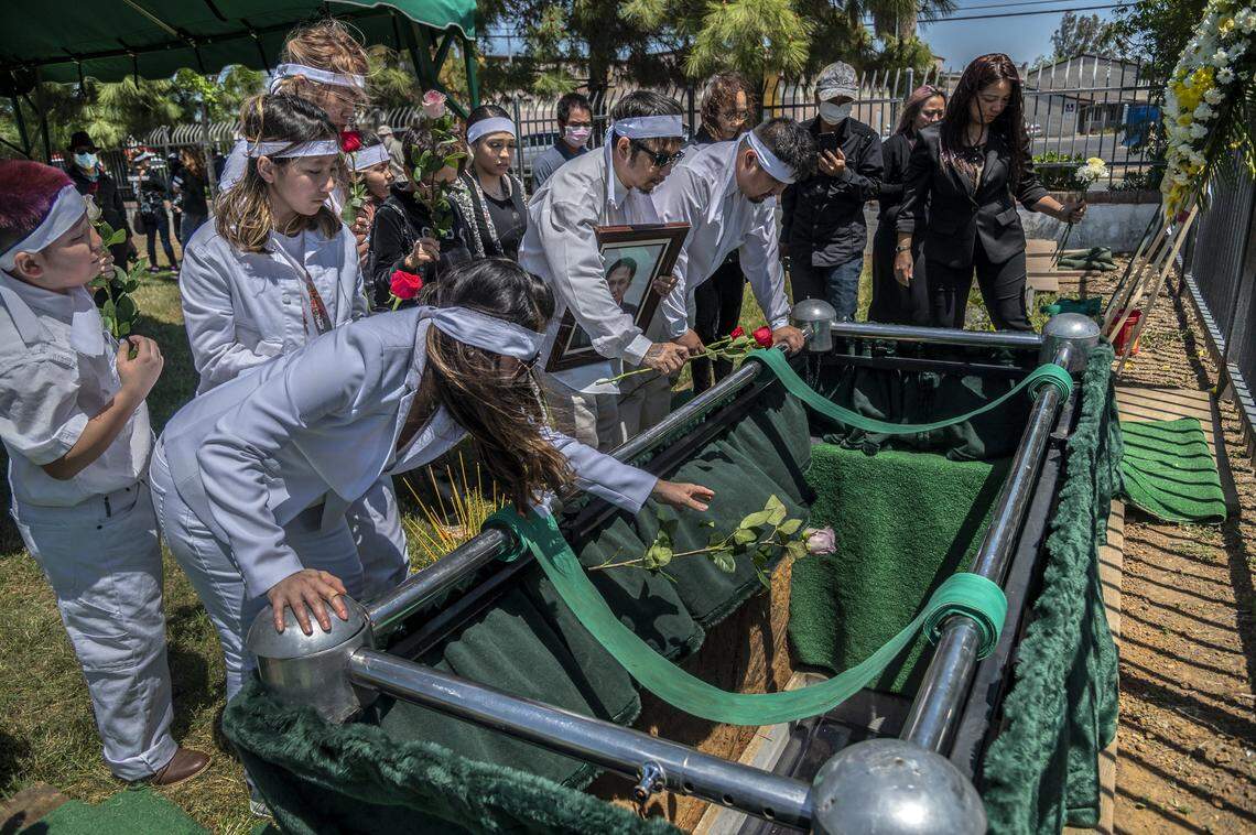 Trang Nguyen, left, throws a rose as the casket is lowered at the funeral of her father-in-law Dung Tan Nguyen on Wednesday, May 6, 2020, during the coronavirus outbreak. Immediate family members, dressed in white, were permitted to approach as a group after the casket was lowered into the grave. All other mourners had to come up in pairs due to social distancing restrictions.