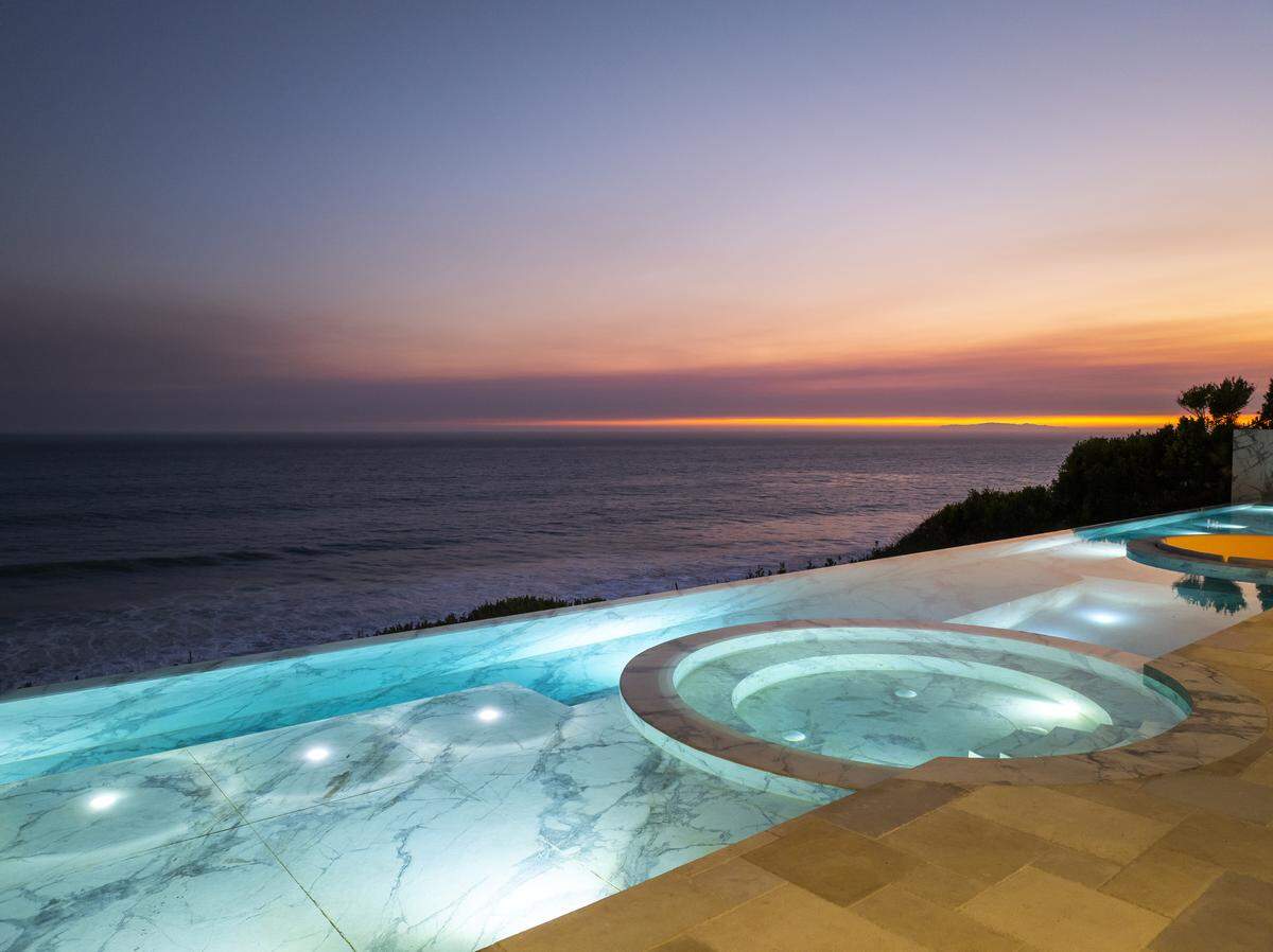 A sweeping multi-level stone pool anchors the ocean-facing terrace, featuring a swim-up bar, sunken lounge and a dramatic window visually merging water with sky.
