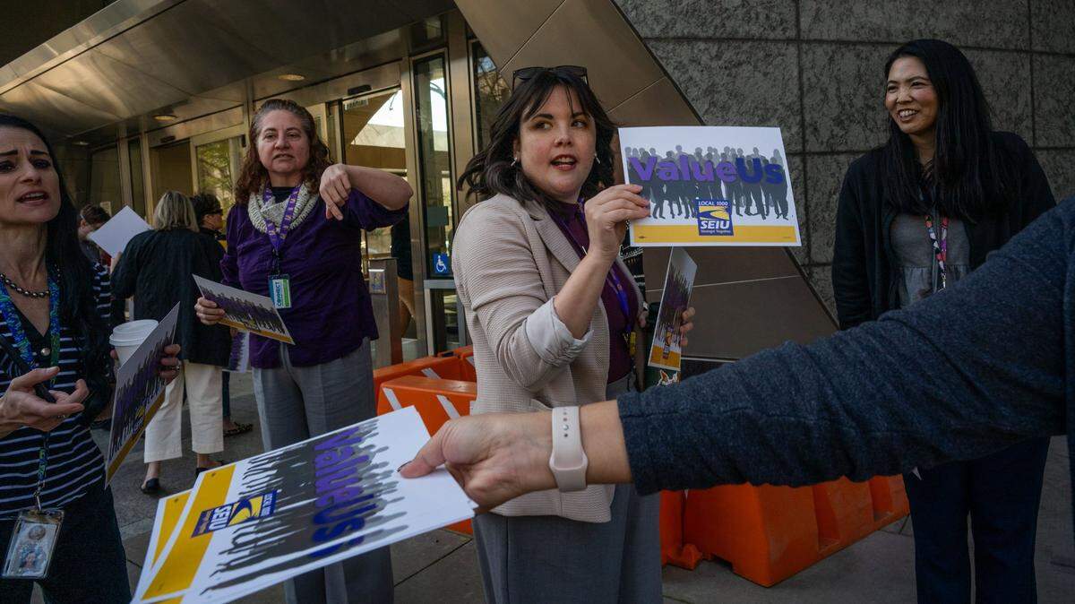 Gina Garcia-Smith, center, a steward for SEIU Local 1000, passes out “Value Us” signs as she and other California Department of Education workers walked out of their offices for a demonstration on Tuesday, March 11, 2025, in downtown Sacramento. They were protesting Gov. Gavin Newsom’s order directing state workers to return to their offices four days a week.

