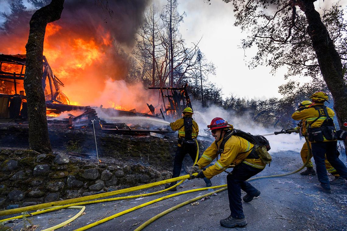 Firefighters battle the Kincade Fire along Highway 128 as a home burns in 2019. A state investigation determined that the fire started when a jumper cable broke on a PG&E transmission line. Almost 400 structures burned in the fire.