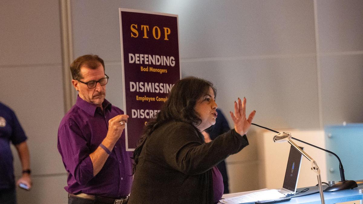 Paulina Vasquez, a lottery sales representative and a member of SEIU Local 1000, speaks Thursday during a California State Lottery Commission meeting about the lack of action on addressing harassment and bullying in the department. Retired worker Russell Sehn holds a sign nearby.