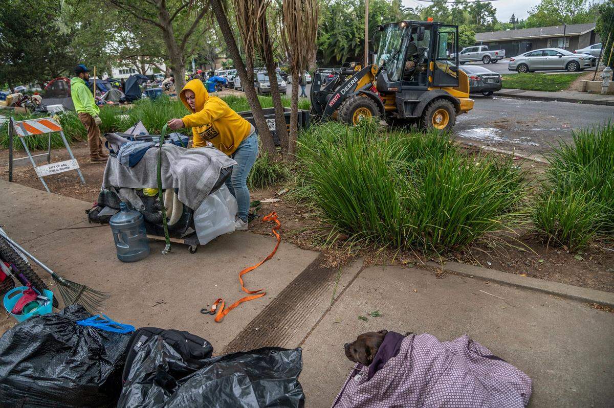 Shelley Sanders, 32, packs her belongings as her dog hides in a blanket, at right, while a bulldozer clears a homeless camp at Fair Oaks Boulevard and Howe Avenue on April 11. She said the campers looked out for each other and finding a shelter with a dog is difficult.