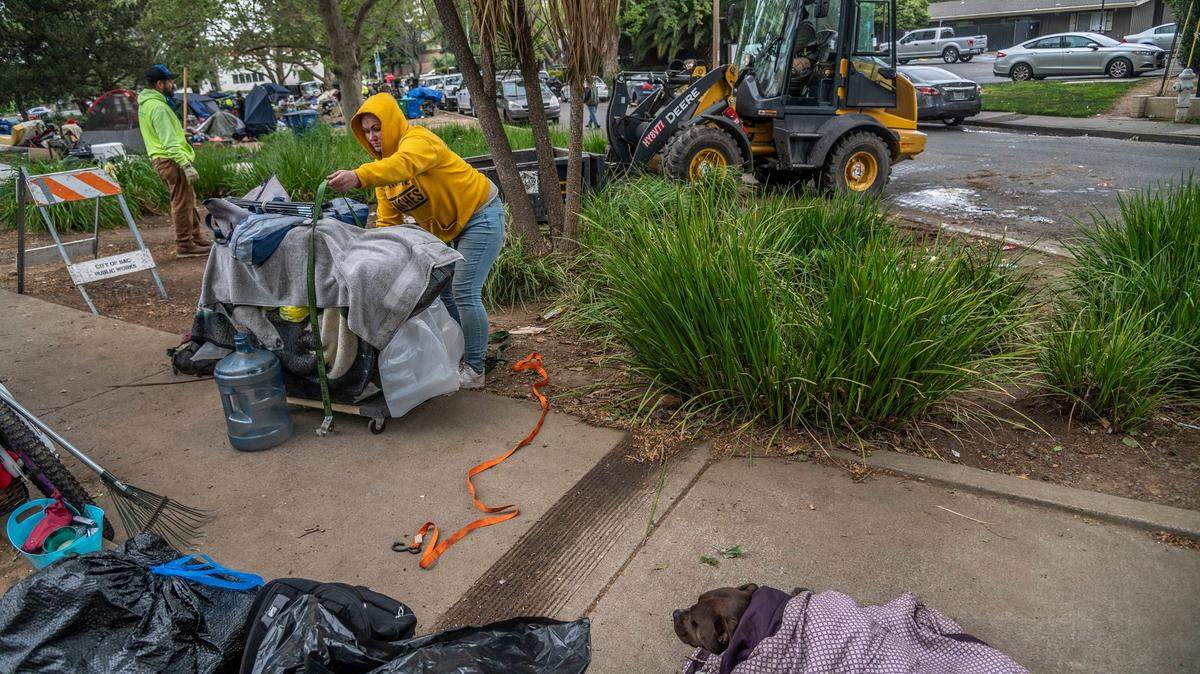 Shelley Sanders, 32, packs her belongings as her dog hides in a blanket, at right, while a bulldozer clears a homeless camp at Fair Oaks Boulevard and Howe Avenue on Monday, April 11, 2022. She said the campers looked out for each other and finding a shelter with a dog is difficult. As a woman, she worries about sexual assaults.