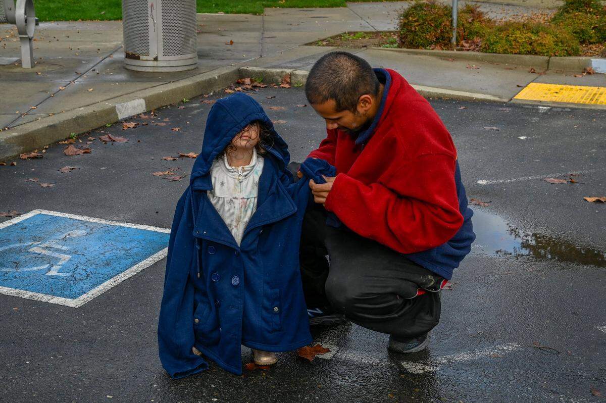 Alfredo Gonzales, helps daughter Gracie, 2, put on an oversized jacket at a park in Rancho Cordova on Thursday, Dec. 9, 2021. The homeless family of five is now living in an SUV because their motorhome was towed away by the city last month and they dont know how to get it back.