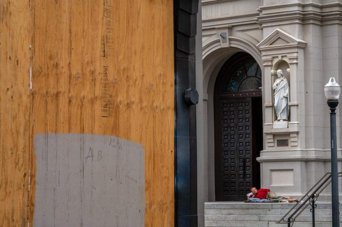 A homeless man rests on top of the steps to the Cathedral of the Blessed Sacrament across from a boarded up storefront on K Street in downtown Sacramento on Thursday.