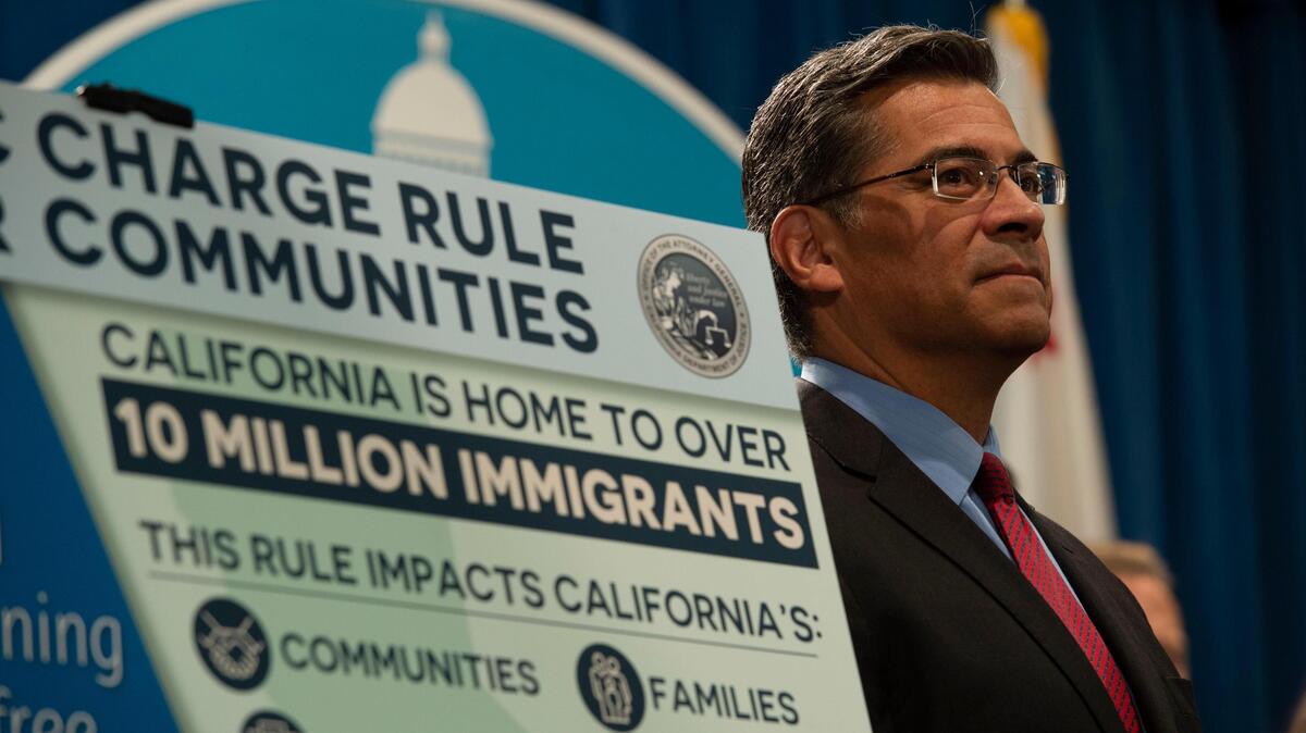 Then-state Attorney General Xavier Becerra stands near the podium during a press conference in 2019 to announce California will file suit against the Trump administration’s ‘public charge’ rule to deny immigrants green cards if they are likely to rely on public benefits.
