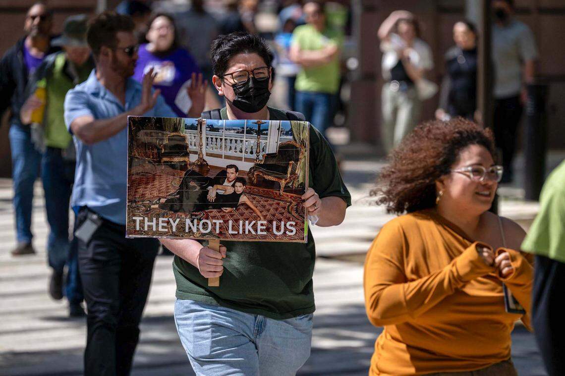 A protester carries a sign featuring a 2004 fashion magazine photograph of Gavin Newsom with first wife Kimberly Guilfoyle and the words “They not like us” during a protest against the governor’s order directing state workers to return to their offices four days a week, at the California Environmental Protection Agency Headquarters in Sacramento on Wednesday.