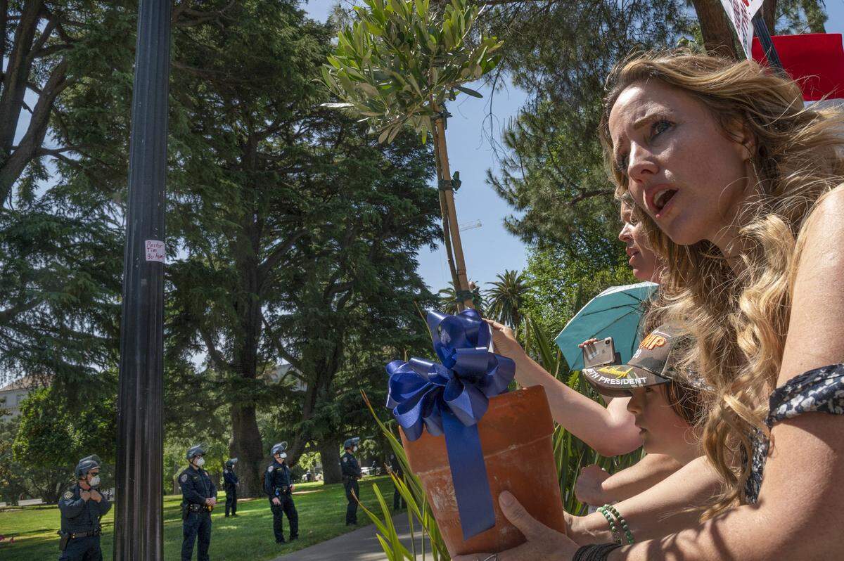 Tara Thornton of the Freedom Angels holds an olive tree for law enforcement officers with Tim Thompson, a conservative pastor from Riverside County, during a protest at the state Capitol on Thursday, May 7, 2020 in Sacramento during the coronavirus pandemic.
