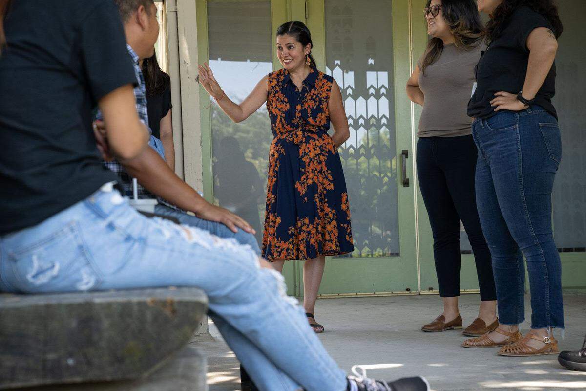 Gabby Trejo, executive director of multi-congregation religious organization Sacramento ACT, talks Friday with members of the group of migrants, left, that were flown to Sacramento from El Paso, Texas, on two flights by a Florida contractor.