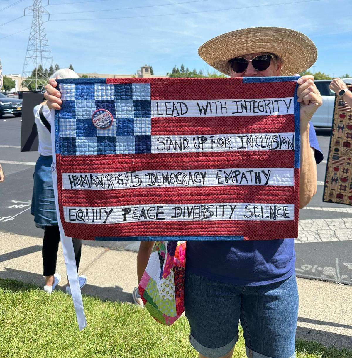 Debra Thompson, 68, carries a quilt she made to hold up as a protest sign at the “No Kings” protest outside the Roseville Galleria.