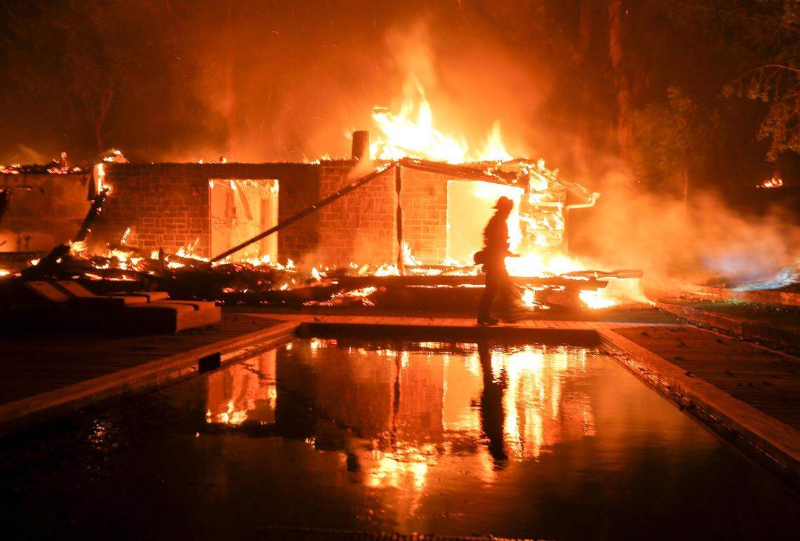 A firefighter walks by the a burning home in Malibu, Calif., Friday, Nov. 9, 2018. A Southern California wildfire continues to burn homes as it runs toward the sea. Winds are blamed for pushing the fire through scenic canyon communities and ridgetop homes. (AP Photo/Ringo H.W. Chiu)