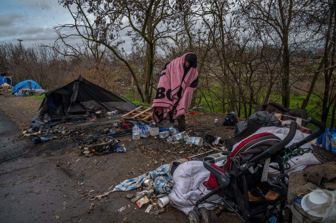 Albert Sorando, 47, wraps in a blanket to stay warm after loosing his tent to a fire Tuesday night during the severe winter storm as he surveys the damage at a homeless encampment near Basler and N. 18th streets in Sacramento on Wednesday, Jan. 27, 2021.