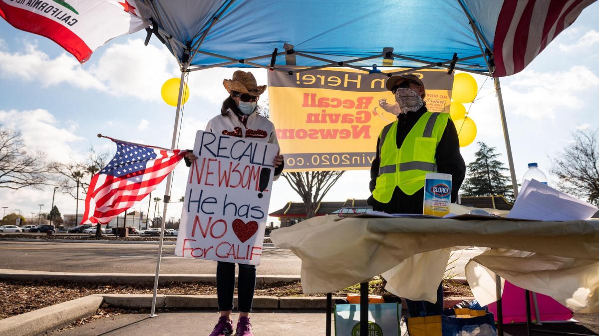 Two women working at the table for the Recall Gavin Newsom campaign, who did not want to be identified, hold signs, answer questions and collect signatures in the parking lot of Rivergate Shopping Center on Saturday, Jan. 23, 2021, in Rancho Cordova.
