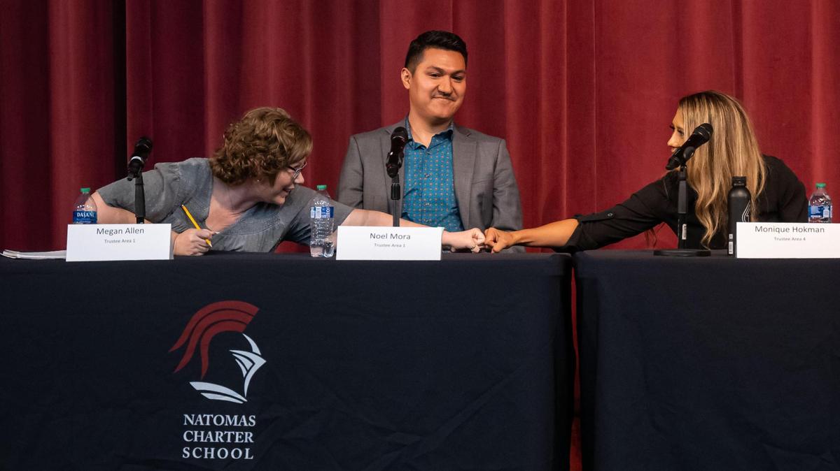 Natomas Unified School District board trustee candidate Megan Allen, left, reaches past her Area 1 opponent Noel Mora, center, to fist bump Area 4 candidate Monique Hokman during intermission in a student-hosted forum Wednesday, Oct. 12, 2022, at the Benvenuti Performing Arts Center adjacent to Natomas Charter School. Hokman is running against Cindy Quiralte.