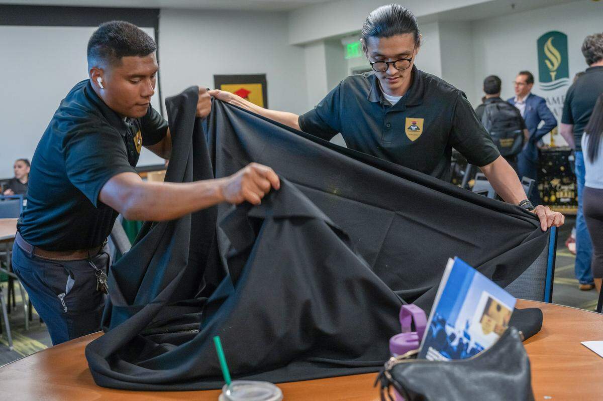 Formerly incarcerated individuals Alfredo “Pasta” Ochoa, left, and Anh-Tuan Pham fold a tablecloth while helping clean up after their Reintegration Academy graduation at Sacramento State on May 9.