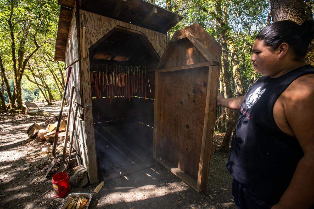 Karuk Tribe member Forrest Davis opens the door to the smokehouse holding salmon caught below the fish camp at Ishi Pishi Falls. “I’ve been the fatavéenaan, the medicine man, here for quite a long time, this is probably one of the first years that I haven’t done it,” he said, referring to important role in the tribe’s annual world-renewal ceremony.