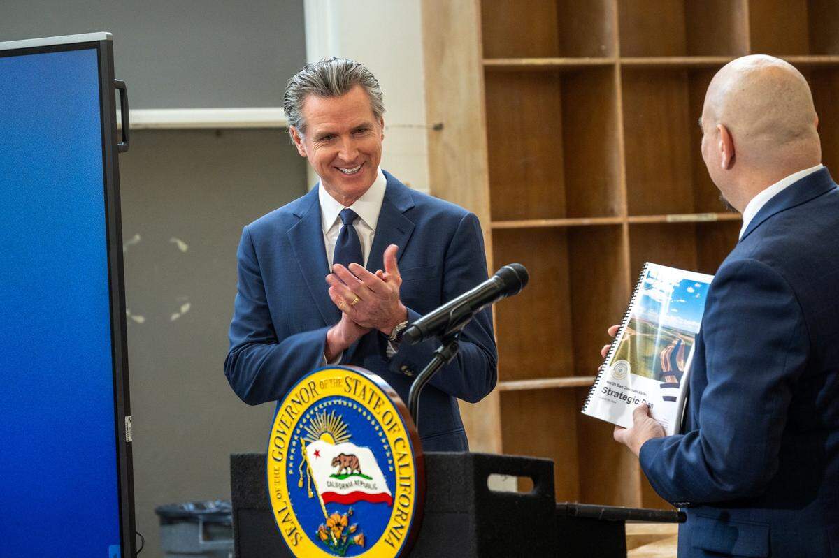 Gov. Gavin Newsom applauds as Erick Serrato, executive director of the Merced County Department of Workforce Investment, presents a strategic plan booklet at a press conference at California State University, Stanislaus in Turlock where he previewed budget toplines on Monday, Jan. 6, 2025.