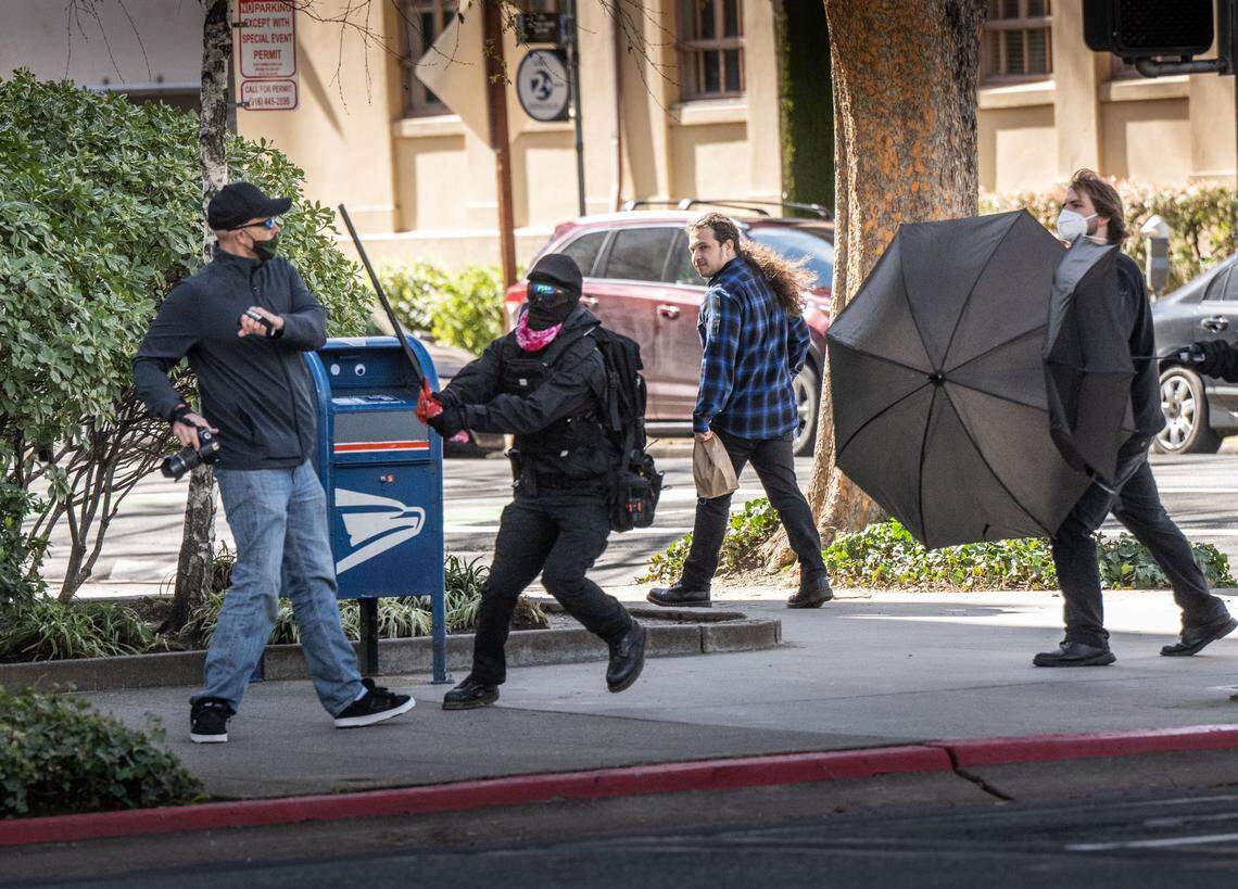 A man carrying a camera is attacked Friday on N Street in Sacramento by a participant in a march by the Pride Was A Riot trans activist group as it moved toward the state Capitol to confront participants in a Detransition Awareness Day event.
