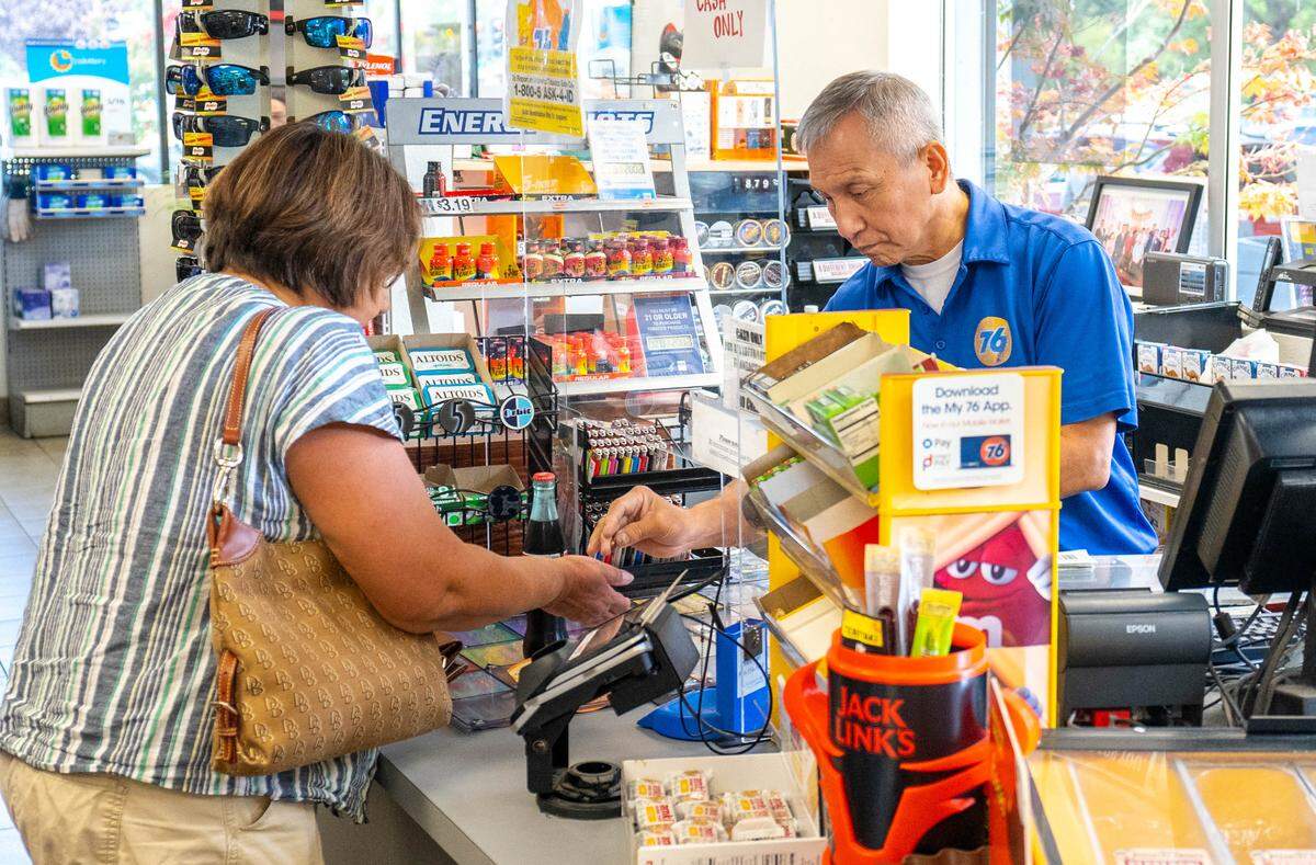 A 76 Gas Station attendant sells a Mega Millions lottery ticket to a customer on Tuesday, August 1, 2023.