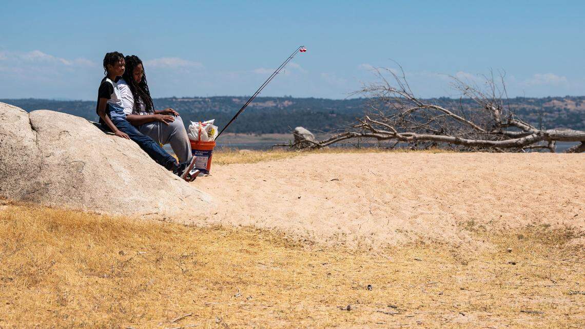 Sharniece Monroe, de Sacramento, se sienta con su hijo, Mizzon Bickham, de 11 años, para descansar en una larga caminata de regreso después de pescar en un día abrasador en el lago Folsom, que se ve como una astilla detrás de ellos el sábado 10 de julio de 2021, ya que alcanzó su nivel mínimo en cinco años, mientras que las temperaturas establecieron un récord en el centro de Sacramento. Monroe dijo que es su primer año pescando juntos. "Es como nuestro tercer, nuestro cuarto viaje, todavía no hemos pescado nada", dijo, sentada en un lugar normalmente sumergido por el lago.