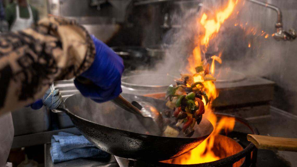 The flame of a gas stove flares up the side of a wok as chef Quan Sun cooks Chinese cuisine at Frank Fats in downtown Sacramento on May 25, 2023.