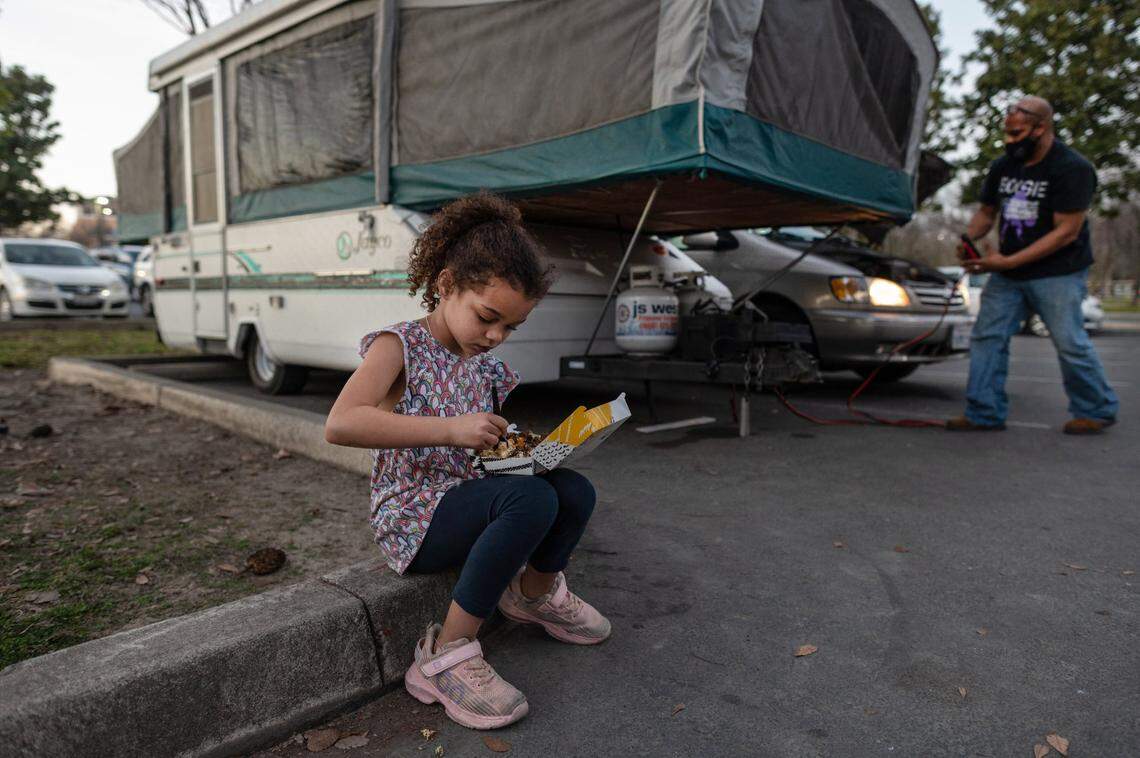 Shyann Slain, 7, eats a meal from Del Taco as her father Anthony Slain hooks up his van’s battery to help heat a camper overnight at a Natomas park in January. The parents say they usually leave the car running all night and sleep in shifts to keep the children warm.