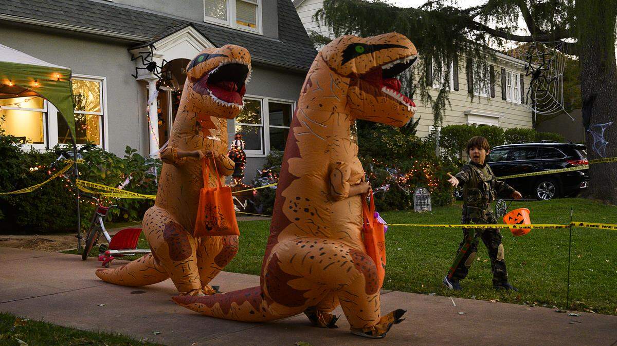 Luke Bassett and Caden Reeves, dressed as dinosaurs, treat or treat in East Sacramento on Thursday, Oct. 31, 2019.