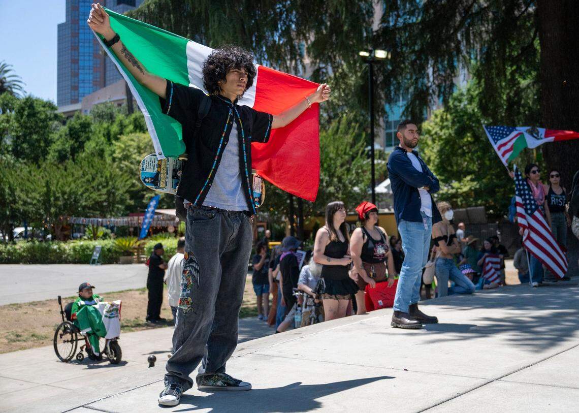 Matthew Loarca stands in Cesar Chavez Plaza holding a Mexican flag during a protest against U.S. Immigration and Customs Enforcement in downtown Sacramento on Monday, June 9, 2025.