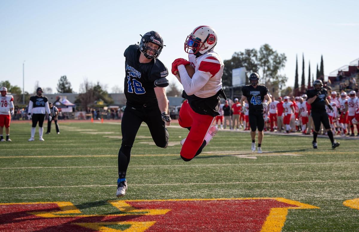 Wide receiver Corey Galindo, with the statewide fire service Fire Dogs, pulls in a touchdown reception in the end zone ahead of defender Jason Rutledge, with the Sacramento region law enforcement Hogs, during the second quarter of the 49th Pig Bowl on Saturday, Jan. 28, 2023, at Hughes Stadium at Sacramento City College. Galindo was named MVP after the Fire Dogs beat the Hogs, 12-5.