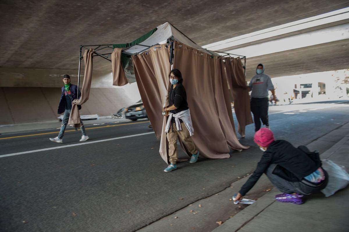 As Sharon Tendarvis, right, picks up trash, volunteers move a tent on from a homeless camp that was being cleared by Caltrans on 29th and G streets in Midtown Sacramento in October 2021. The agency wants more than $5 million to clear thousands of homeless encampments around the state.