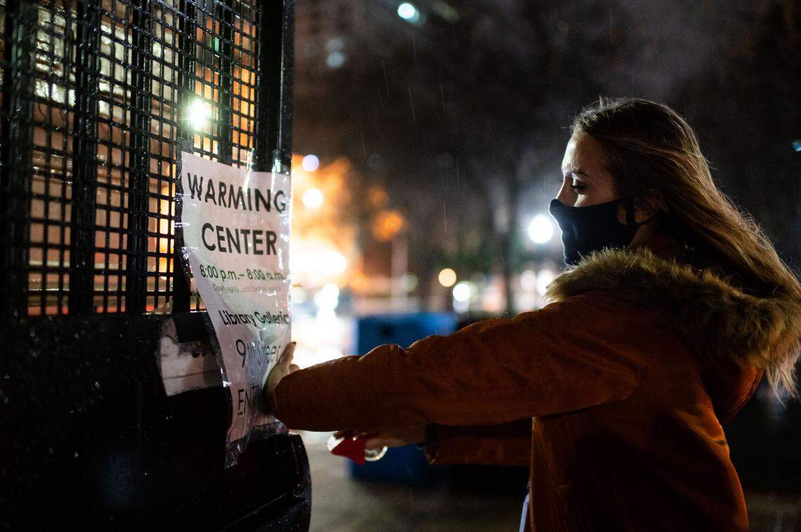 Lauren Groves, an Emergency Operations Center coordinator with the City of Sacramento, tapes up a sign for the opening of the warming center at Tsakopoulos Library Galleria outside the entrance on 9th Street across from Cesar Chavez Plaza on Wednesday, Jan. 27, 2021, in downtown Sacramento. City officials said it will be open 8 p.m. to 8 a.m. until further notice.