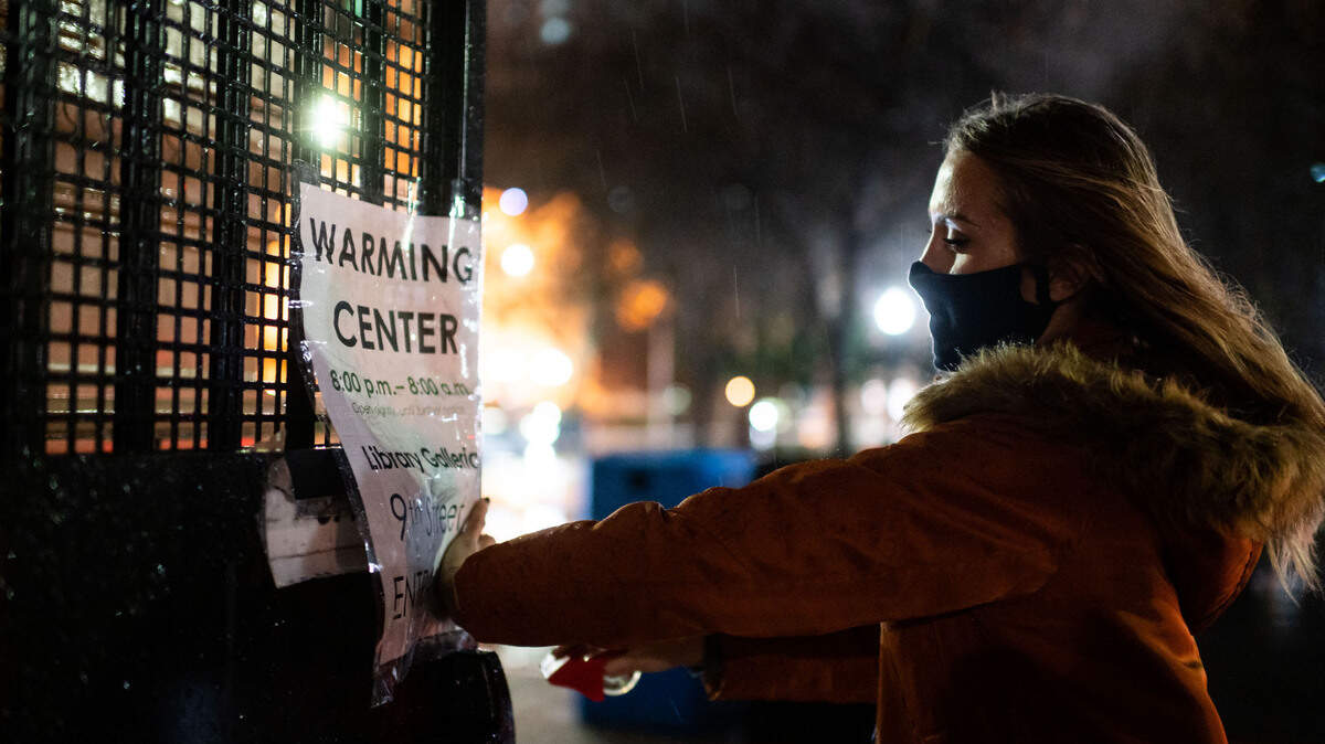 Lauren Groves, una coordinadora del Centro de Operaciones de Emergencia de la Ciudad de Sacramento, pega un cartel para la apertura del centro de calentamiento en la Tsakopoulos Library Galleria fuera de la entrada en 9th Street frente a la César Chávez Plaza el miércoles 27 de enero de 2021, en el centro de Sacramento. Los funcionarios de la ciudad dijeron que estará abierto de 8 p.m. a 8 a.m. hasta nuevo aviso.