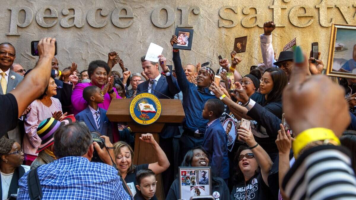 California Governor Gavin Newsom holds up a copy of Assembly Bill 392 after signing it on Monday, Aug.19, 2019 in Sacramento. To his right, Stevante Clark holds a picture of his brother Stephon Clark and his family, as Clark’s grandmother Sequita Thompson smiles holding a photo below. Left of Newsom is Assemblymember Shirley Weber (D-San Diego), who authored the bill that limits use of force by police.