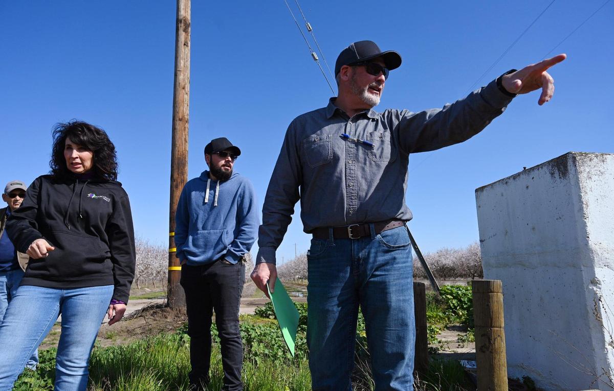 Madera Irrigation District engineering tech Darren Garcia, right, points off to the distance as he discusses the basin with Jennifer Peters of Markarian Family LP, left, and Kevin Markarian, center, Friday, March 3, 2023 near Madera.