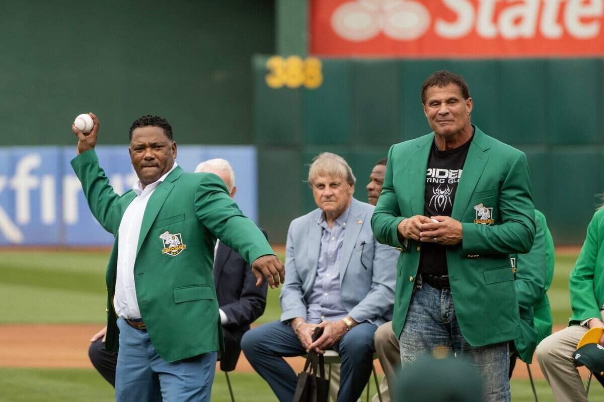 Miguel Tejada, left, and José Canseco throw out the ceremonial first pitch after the two were inducted into the Oakland Athletics Hall of Fame last month.