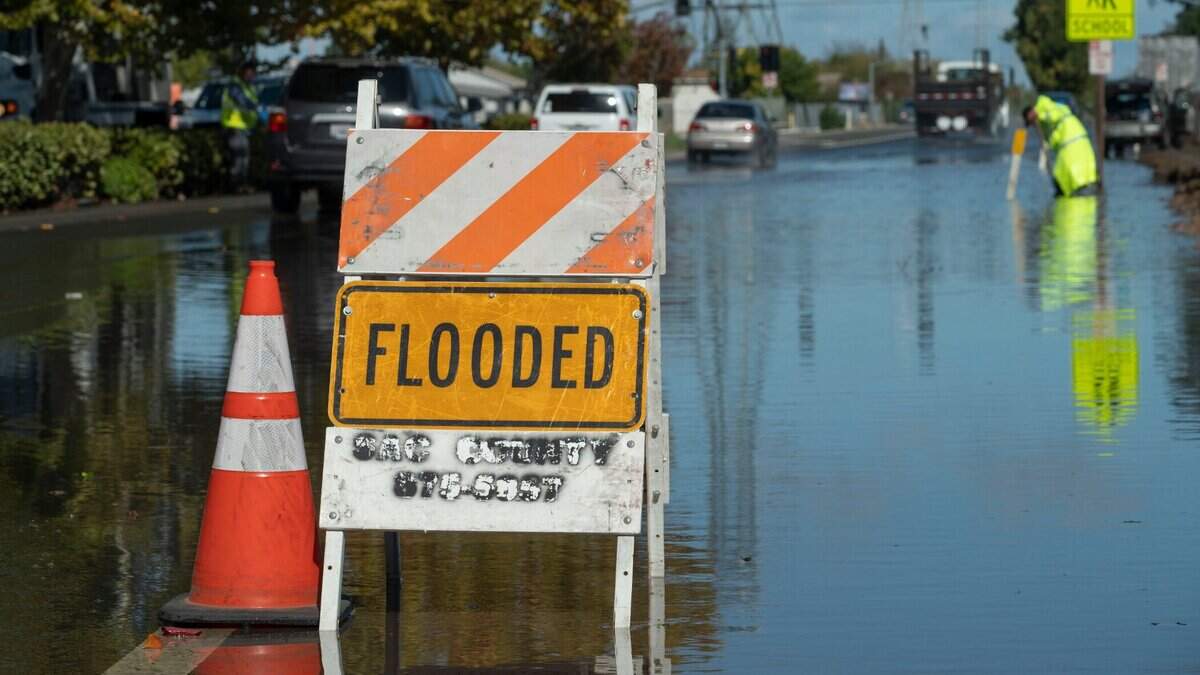 A flooded sign warns motorist as Andre Dominguez a storm utility worker for Sacramento County attempts to open a drain on Power Inn Rd. Near Stevenson Ave. on Monday, Oct. 25, 2021 a day after a storm brought more than five inches of rain to the area.