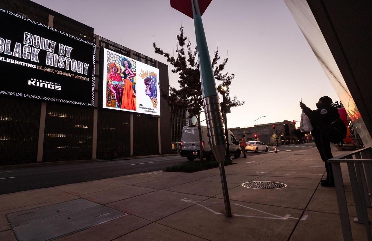 Margaret Mwansa, of Sacramento, stops to take a photo outside Golden 1 Center on Friday, Feb. 5, 2021, of Christopher Williams’ artwork, which was curated by Black Artists Fund for the Sacramento Kings to commemorate Black History Month. “It’s really beautiful, the art is really amazing,” she said, “I like it.”
