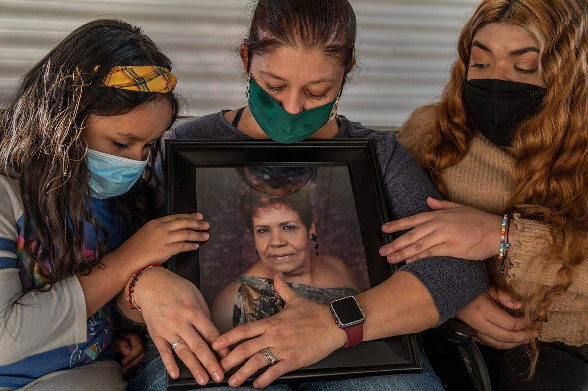 With her mask stained with tears, Norma Galindo on Tuesday, Dec. 1, 2020, holds a portrait of her mother Hermelinda Ruiz, 67, who died of COVID-19. Her daughters Dulcenoemi Galindo, 7, left, and Miranda Villarreal, 18, also had the virus.