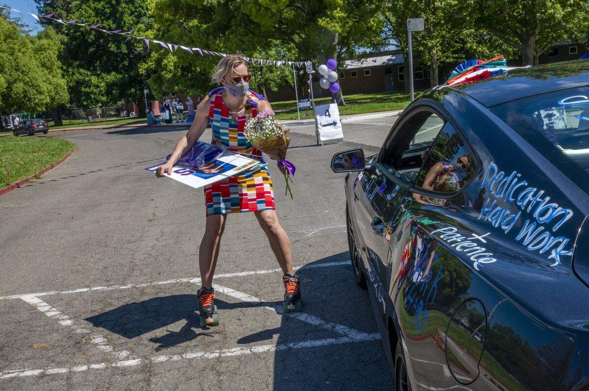 A masked Andrea Smith, culture and operations coordinator at Sacramento Charter High School, roller skated up to cars as she passed out graduation caps and gowns, flowers and lawn posters with senior portraits on them to the class of 2020 graduates on Wednesday, May 27, 2020, during the coronavirus outbreak.