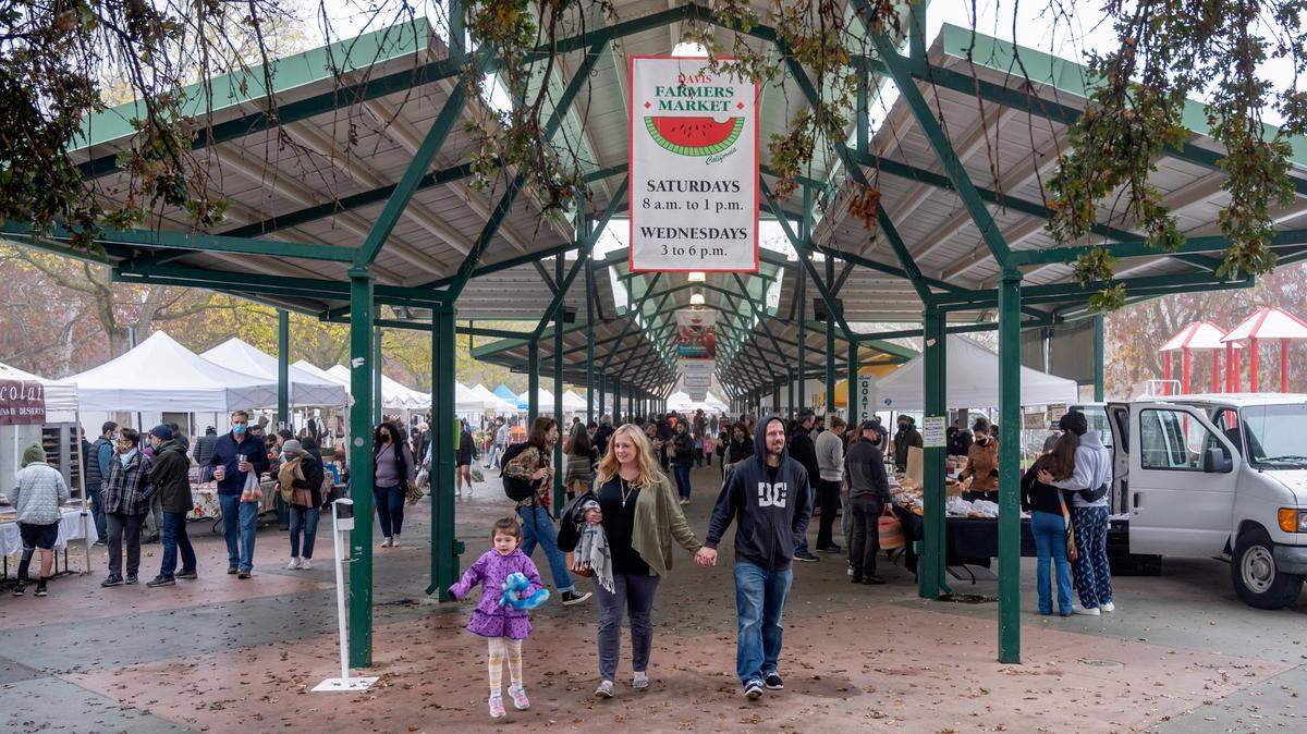 Kristen Patchett, center, of Sacramento, walks with Tim Thixton and his daughter Grace, 5, at the Davis Farmers Market at Central Park in Davis on Saturday, Dec. 4, 2021. Patchett said she used to go to UC Davis and likes to come back to her old stomping grounds.