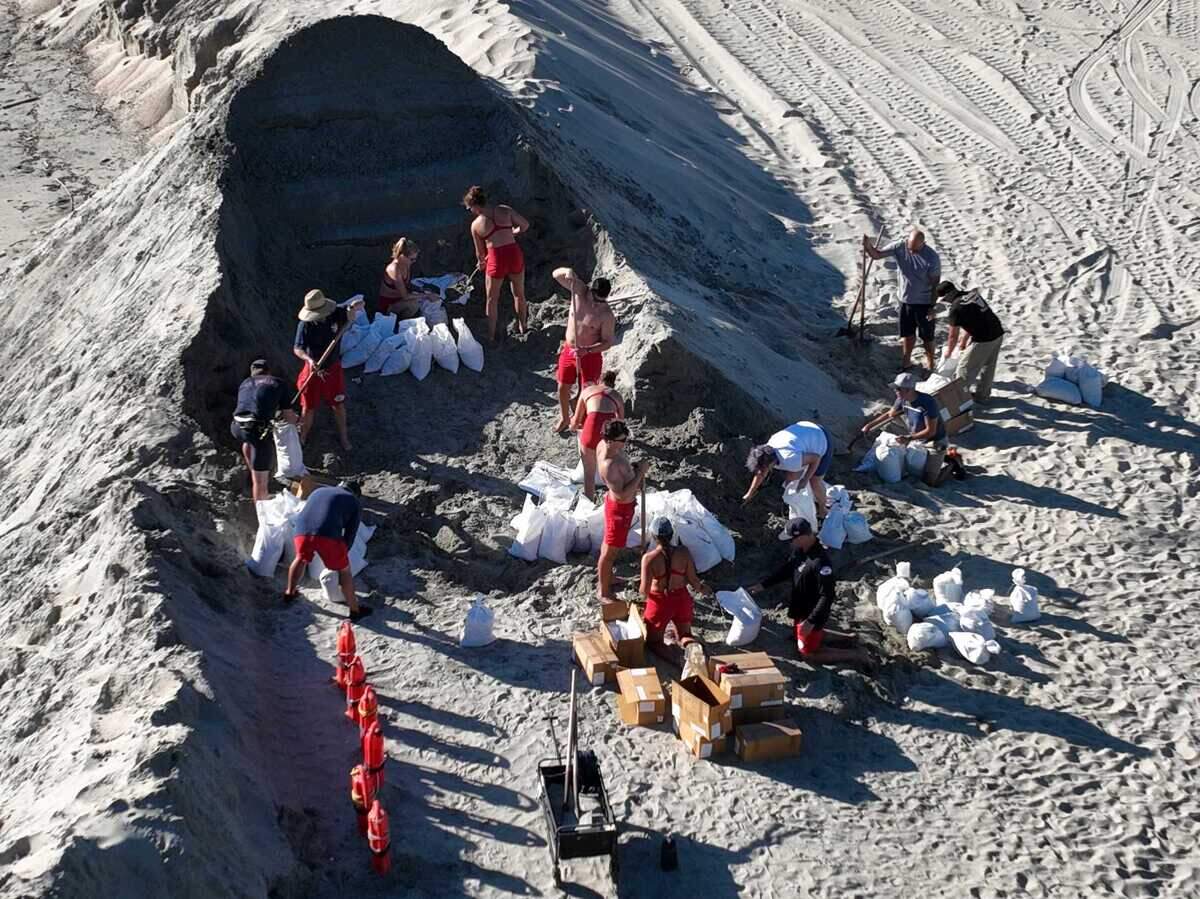 Long Beach lifeguards fill sandbags to help residents fortify their homes for the remnants of Hurricane Hilary while crews build a sand berm along the shore near Alamitos Bay on Friday.