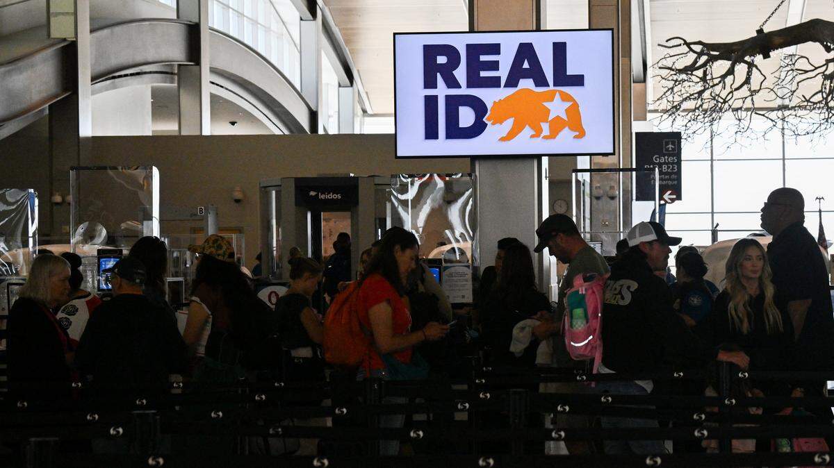 Travelers wait in line to pass through security and TSA screen under a sign reading "Real ID" at Sacramento International Airport in 2025. Real ID is a federally mandated form of identification in the US that meets enhanced security standards set by the Department of Homeland Security.